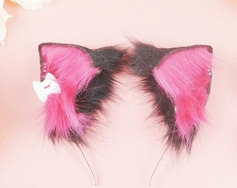 May include: A pair of black and pink cat ears headband with a white bow. The headband is made of faux fur and has a wire frame.