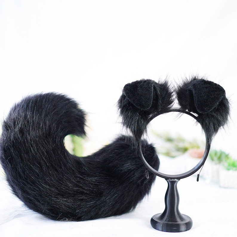 May include: Black furry cat ears headband and a matching black furry tail. The headband is on a black stand.