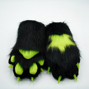 Puede incluir: Un par de patas peludas negras con garras verdes y detalles verdes. Las patas tienen un dise&ntilde;o en forma de estrella en la parte posterior.