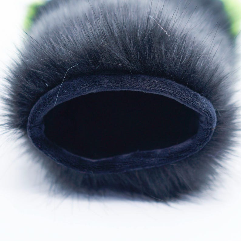 May include: Black faux fur microphone wind screen with a dark blue velvet lining. The wind screen is designed to reduce wind noise when recording audio.