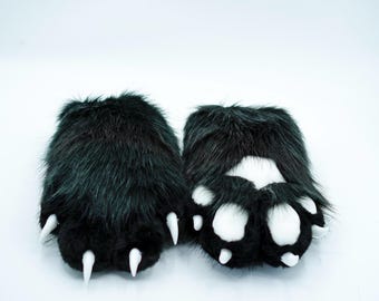 Puede incluir: Un par de patas peludas negras con almohadillas blancas y garras negras. Las patas están hechas de tela suave y de felpa y están diseñadas para parecer patas de animales.