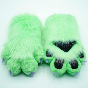 May include: A pair of green furry paw hand puppets with purple claws. The paws have black felt paw pads.