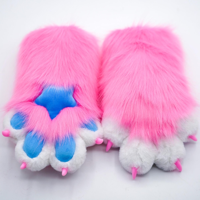 Puede incluir: Un par de calentadores de manos de pata peluda rosa con almohadillas de pata azules y garras rosas.
