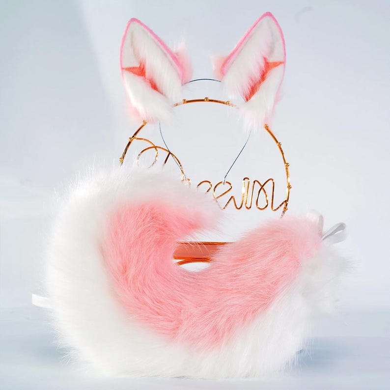 May include: A fluffy pink and white fox tail with matching pink and white ears. The tail is curled up and the ears are standing up. The tail and ears are on a gold wire stand.