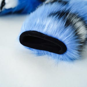 May include: Close-up of a blue faux fur sleeve with black and white accents. The interior cuff is black. The fur is long and fluffy, with a soft texture. The sleeve is likely part of a costume or accessory.