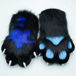 May include: A pair of black furry paws with blue paw pads. One paw has a blue patch on the top.