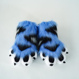 May include: A pair of blue and black faux fur paws with white paw pads and black claws. The furry paws are designed to resemble animal feet. The paws are set against a white background.