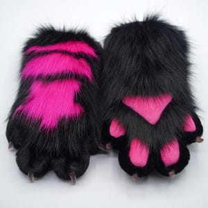 May include: A pair of black furry paw hand warmers with pink accents. The paw pads are pink and the fur is black.