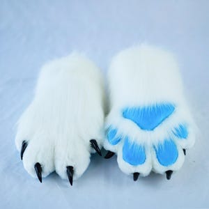 May include: A pair of white furry paws with black claws. One paw has blue paw pads, the other has plain white pads.