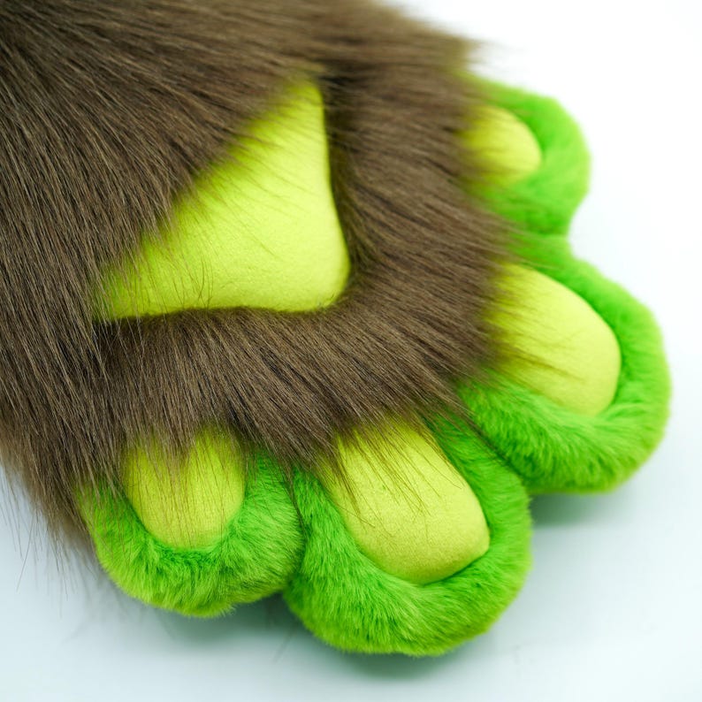 May include: Close-up of a brown furry paw with green felt paw pads. The paw pads have a light green center and a darker green border.
