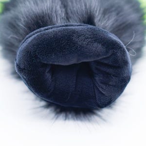 May include: Close-up of the inside of a black faux fur pom pom hat. The hat is lined with a soft, dark blue fleece fabric.