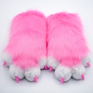 Puede incluir: Un par de pantuflas de pata peludas de color rosa con almohadillas de pata blancas y garras rosas.