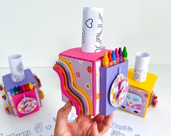 May include: A colorful, multi-layered cardboard box with a groovy theme. The box is decorated with rainbows, flowers, and a peace sign. It has a slot for crayons and a roll of paper. The box says "Don't is Two Groovy" on the side.