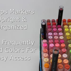Open box of acrylic markers with some sticking up higher because of the inserts making it easier to access them while coloring. The text overlaid on the image says Keeps Markers Upright & Organized. Flip Frequently Used Colors for Easy Access.