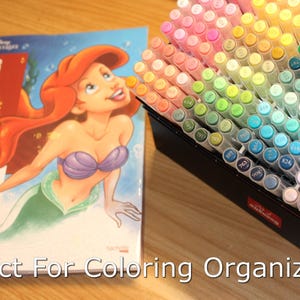 Coloring book with Princess Ariel on the cover sitting on a desk next to open box of acrylic paint markers. Text overlaid on the image says Perfect For Coloring Organization.
