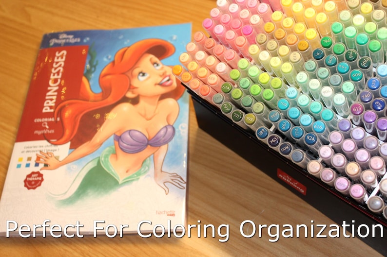 Coloring book with Princess Ariel on the cover sitting on a desk next to open box of acrylic paint markers. Text overlaid on the image says Perfect For Coloring Organization.