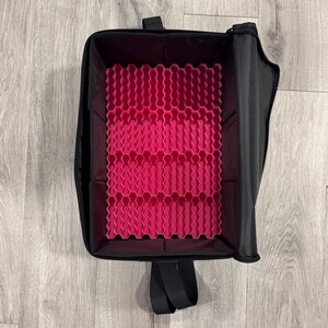 May include: Black makeup case with a bright pink honeycomb-patterned interior. The case has a zippered closure and a handle. The interior is designed to hold and organize various beauty products. The case is open, revealing the interior.