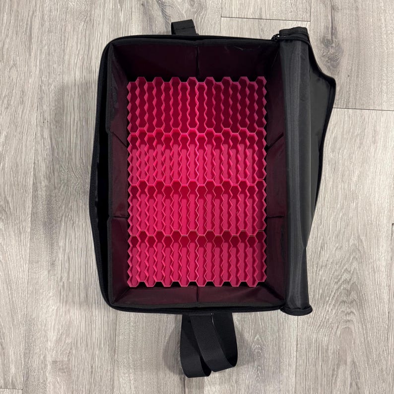 May include: Black makeup case with a bright pink honeycomb-patterned interior. The case has a zippered closure and a handle. The interior is designed to hold and organize various beauty products. The case is open, revealing the interior.