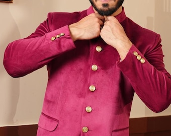 Könnte beinhalten: Ein magentafarbener Samtblazer mit goldenen Knöpfen und einem Stehkragen. Die Jacke hat zwei Vordertaschen und wird mit einer weißen Hose kombiniert. Die Ärmel haben drei goldene Knöpfe. Der Blazer ist ein formeller Stil.