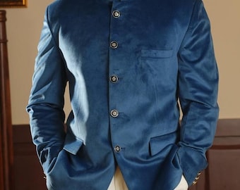 Könnte beinhalten: Türkisblaue Samtjacke mit Stehkragen und vier dunklen Knöpfen. Dazu eine cremefarbene Hose und schwarze Loafer. Das Outfit ist ein formelles Ensemble.
