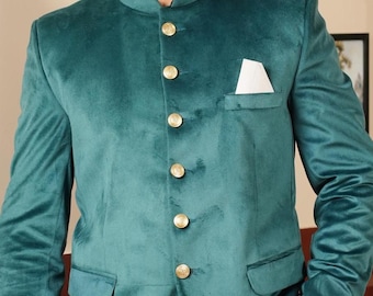 Könnte beinhalten: Türkisblauer Samtblazer mit Stehkragen und goldenen Knöpfen. Die Jacke hat eine Brusttasche mit weißem Einstecktuch. Kombiniert mit einer weißen Hose. Festliche Kleidung.