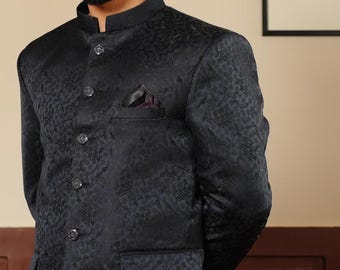 Könnte beinhalten: Ein schwarzer Blazer mit Muster, Stehkragen und Einstecktuch. Der Blazer hat ein dezentes Blumenmuster und ist zugeknöpft. Das Kleidungsstück ist Teil einer formellen Bekleidungskollektion.