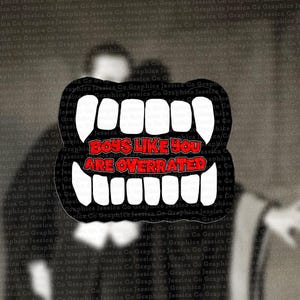 Op de afbeelding: Een zwarte sticker met witte vampiertanden en de rode tekst "BOYS LIKE YOU ARE OVERRATED" tegen een vage grijstinten achtergrond. De sticker heeft een zwarte rand en een onregelmatige vorm.