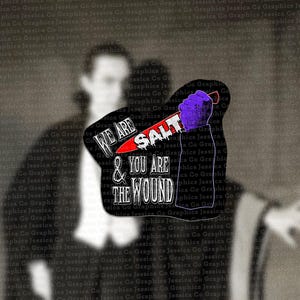 Op de afbeelding: Een zwart-wit afbeelding met een grafisch ontwerp. Het ontwerp toont een paarse hand die een mes vasthoudt met het woord "SALT" op het lemmet. Tekst luidt "WE ARE & YOU ARE THE WOUND".