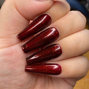 May include: Long, red, glitter nail tips with a glossy finish.