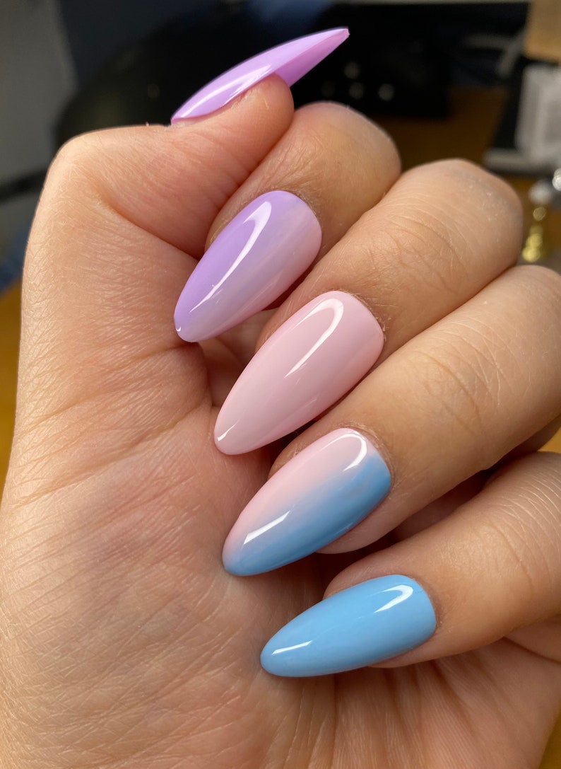 May include: A set of five long, almond-shaped press-on nails with a gradient ombre design. The nails are painted in shades of light blue, pink, and purple.