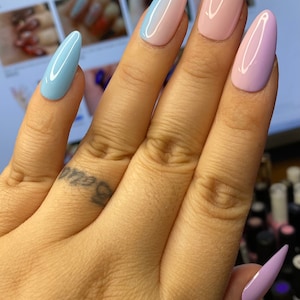 May include: Close-up of a hand with long, almond-shaped nails painted in a pastel ombre design. The nails are painted in shades of light blue, pink, and lavender.