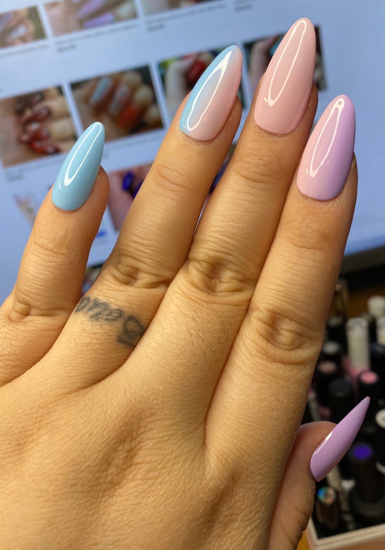 May include: Close-up of a hand with long, almond-shaped nails painted in a pastel ombre design. The nails are painted in shades of light blue, pink, and lavender.