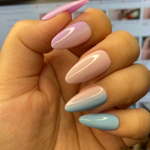 May include: A set of five long, almond-shaped false nails with a gradient ombre design. The nails are painted in shades of light blue, pink and purple.
