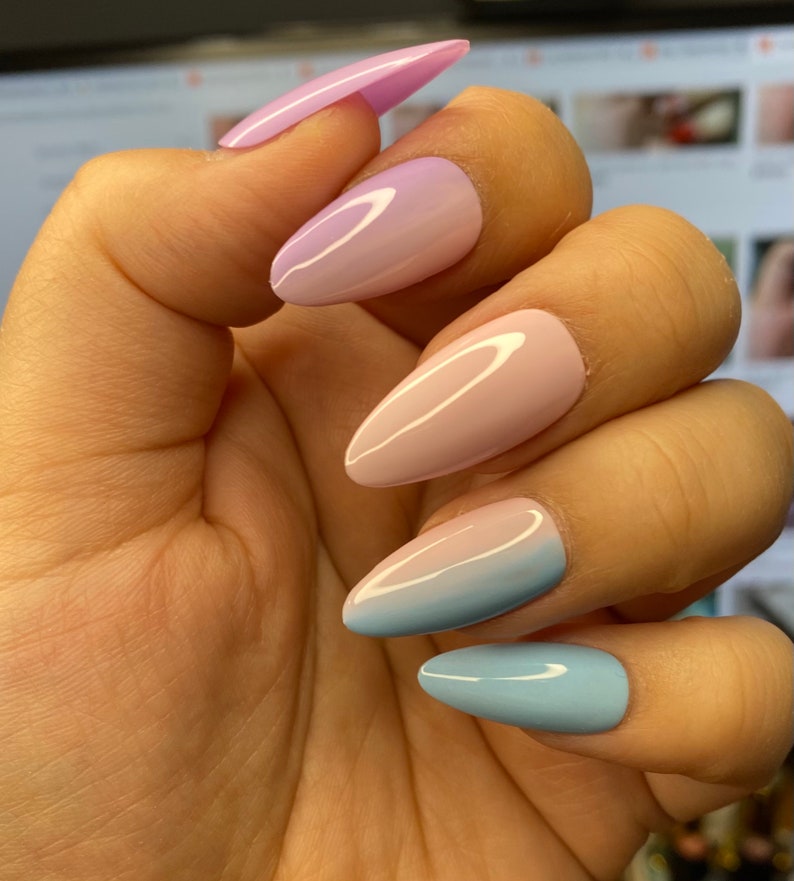 May include: A set of five long, almond-shaped false nails with a gradient ombre design. The nails are painted in shades of light blue, pink and purple.