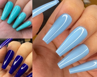 May include: Close-up of hands with long, light blue and dark blue acrylic nails. The nails are long and pointed, with a glossy finish.