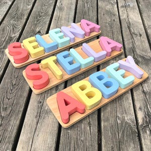 May include: Three wooden puzzle boards with colourful letters spelling out the names "SELENA", "STELLA", and "ABBEY".