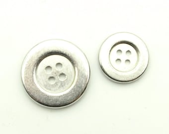 Op de afbeelding: Twee zilveren metalen knopen met elk vier gaten. De grotere knop is ongeveer 2,5 cm in diameter en de kleinere knop is ongeveer 1,25 cm in diameter.