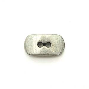 May include: A silver-toned, rectangular button with two holes. The button has a slightly textured surface.