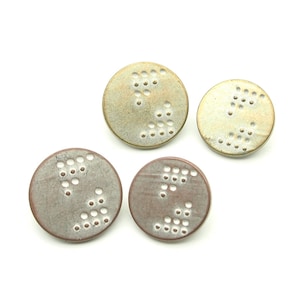 May include: Four round ceramic earrings with a textured surface and a pattern of small holes. The earrings are in shades of gold and brown.