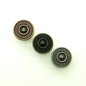 May include: Three round metal buttons with a raised center and concentric circles. The buttons are in shades of copper, bronze, and silver.