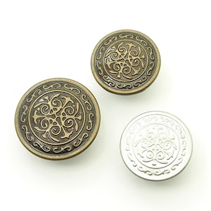 Può includere: Tre bottoni rotondi decorativi con un design ornato e a spirale. Due bottoni hanno una finitura bronzo, mentre il terzo è argentato. Questi bottoni sono probabilmente per abbigliamento o progetti artigianali.