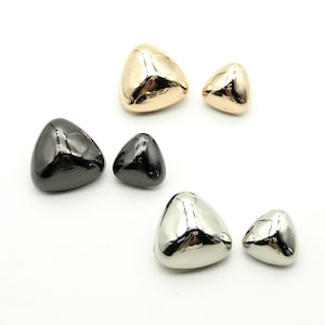 May include: Three pairs of triangle-shaped metal buttons in gold, black, and silver.