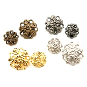 Könnte beinhalten: Sortiment an dekorativen, metallenen Blumenverzierungen in Gold-, Silber- und Bronzetönen. Die Verzierungen haben ein zartes, filigranes Design mit durchbrochenen Details.