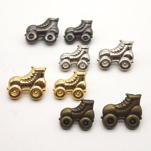 May include: A collection of roller skate charms in various metallic finishes. The charms are in shades of gold, silver, bronze, and gunmetal. Each charm features a detailed roller skate design with four wheels.