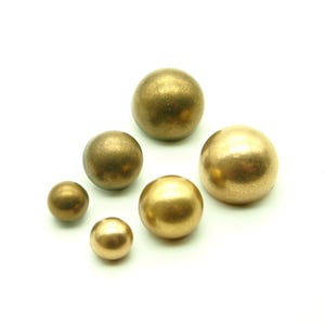 Puede incluir: Seis esferas de color bronce de diferentes tamaños sobre un fondo blanco. Las esferas tienen un acabado liso y metálico. Los tamaños varían, de pequeños a grandes, creando una disposición visualmente interesante.