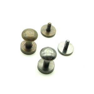 May include: Three metal button fasteners, two are brass colored and one is silver colored. The fasteners have a round head and a threaded post.
