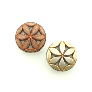 Könnte beinhalten: Zwei runde Dekorknöpfe mit geometrischem Blumenmuster. Ein Knopf ist kupferfarben und der andere goldfarben.