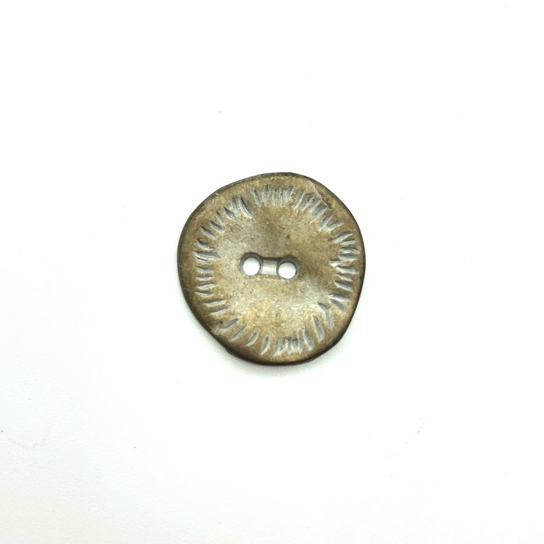 Pode incluir: Um bot&atilde;o redondo de dois furos, de cor castanho, com um design branco texturizado em torno da borda.