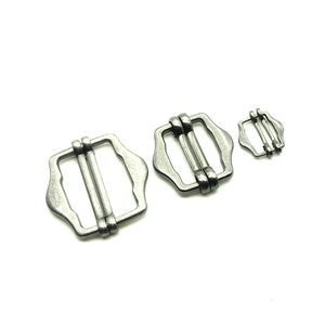 May include: Three silver-toned metal slider buckles of different sizes. The buckles are rectangular with rounded corners and have a smooth, polished finish.