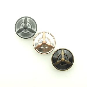 May include: Three metal buttons with a propeller design. The buttons are in black, silver, and copper.